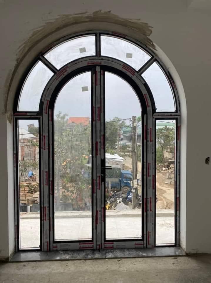 Cửa nhôm kính khung đen dạng vòm lớn đang lắp đặt trong nhà nhìn ra công trình bên ngoài